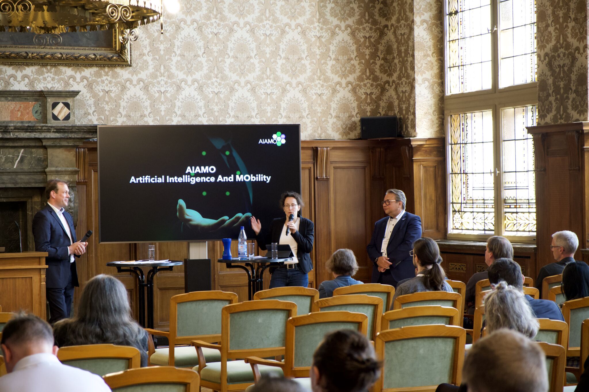 Image of a talk of AIAMO project in front of the audience at Ratsplenarsaal.